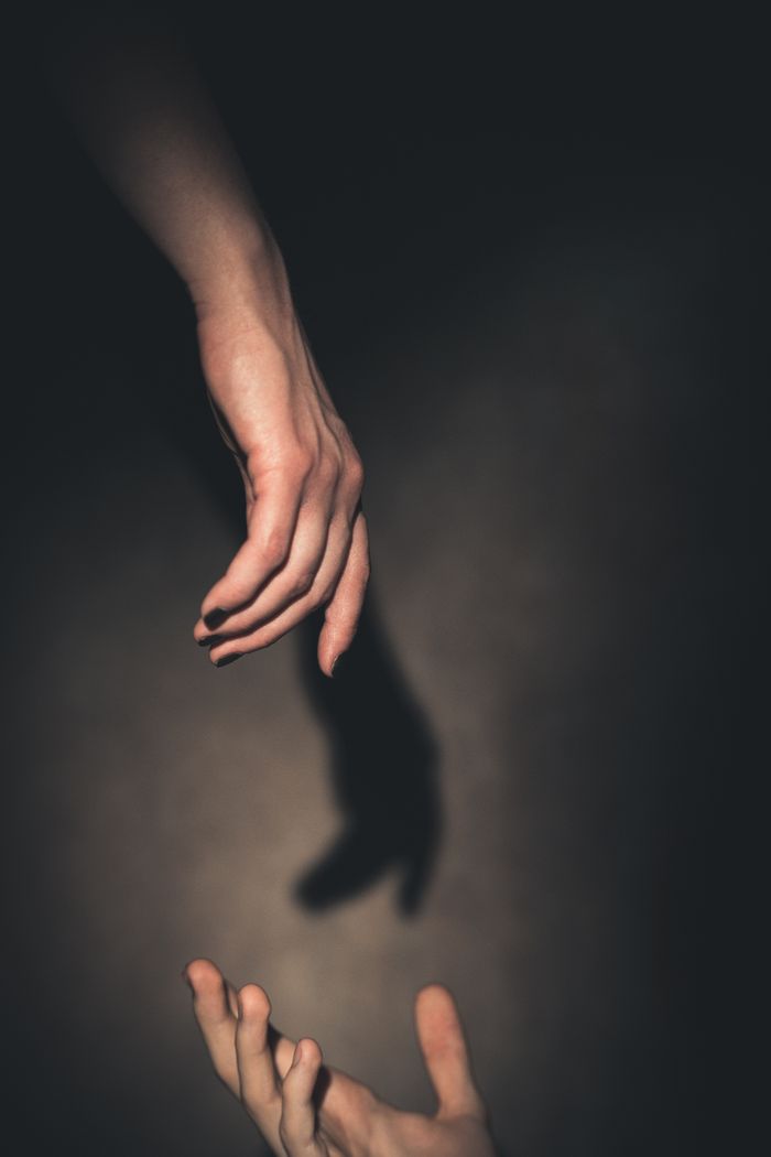 A compelling artistic photo of two hands reaching with dramatic shadows.