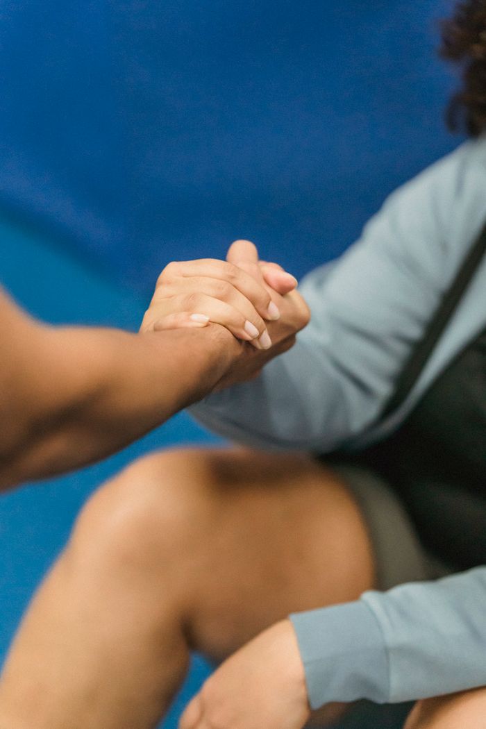 From above of crop unrecognizable trainer giving hand to anonymous overweight female sitting on floor after workout